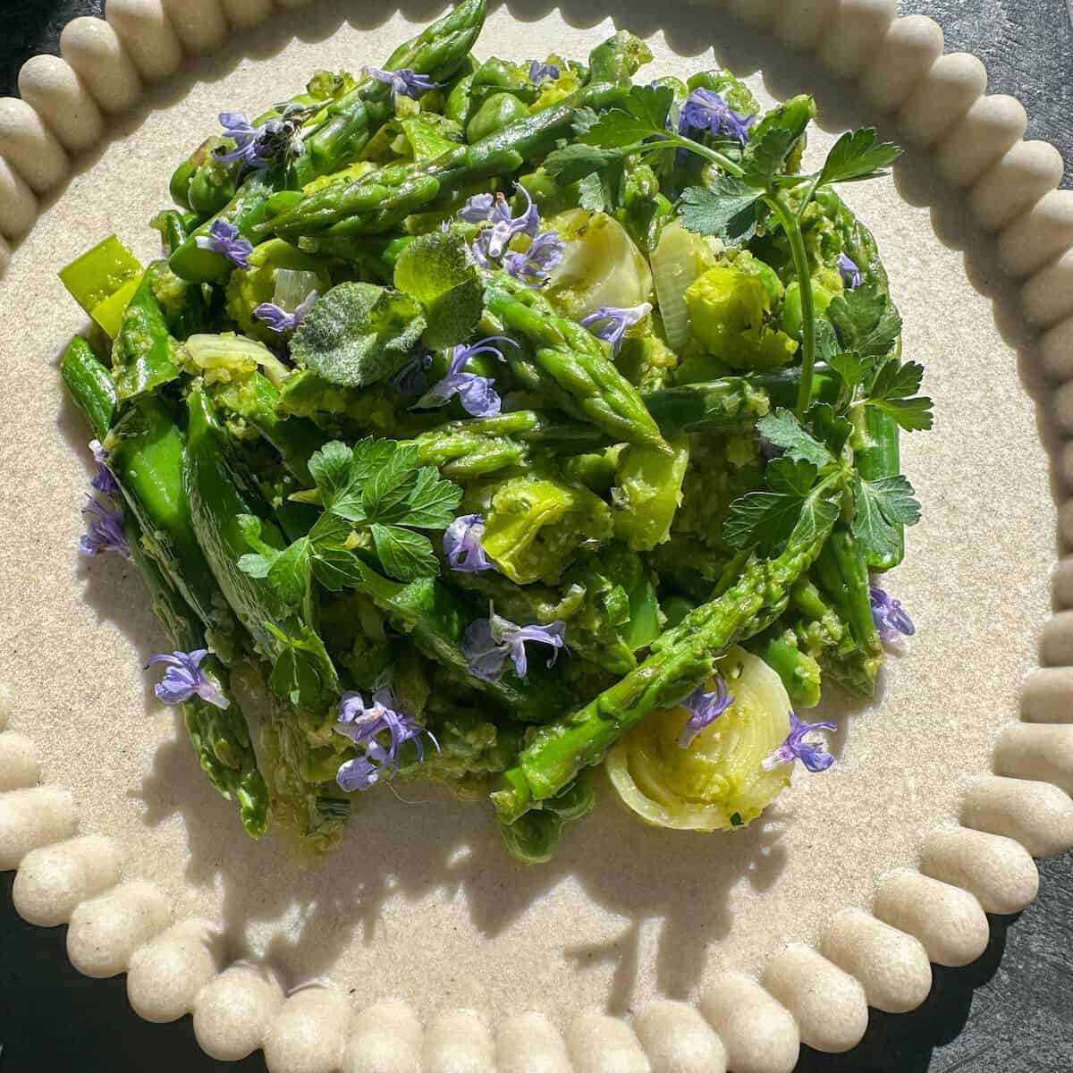 A plate of spring vegetable fricassee with purple edible flowers. 