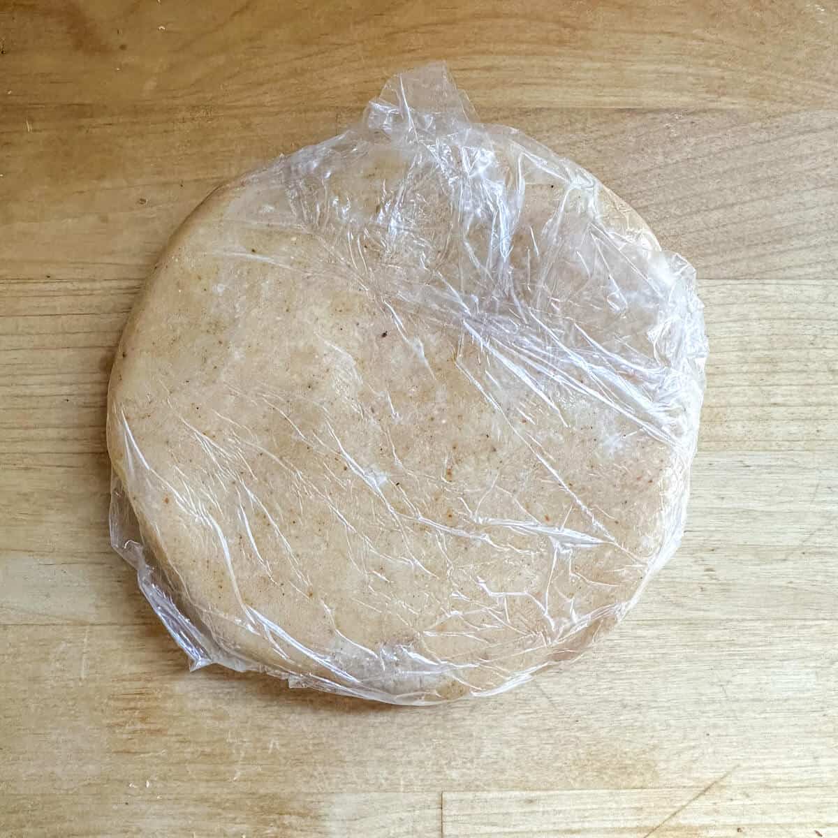 A disk of parmesan sable dough wrapped in plastic food wrap. 