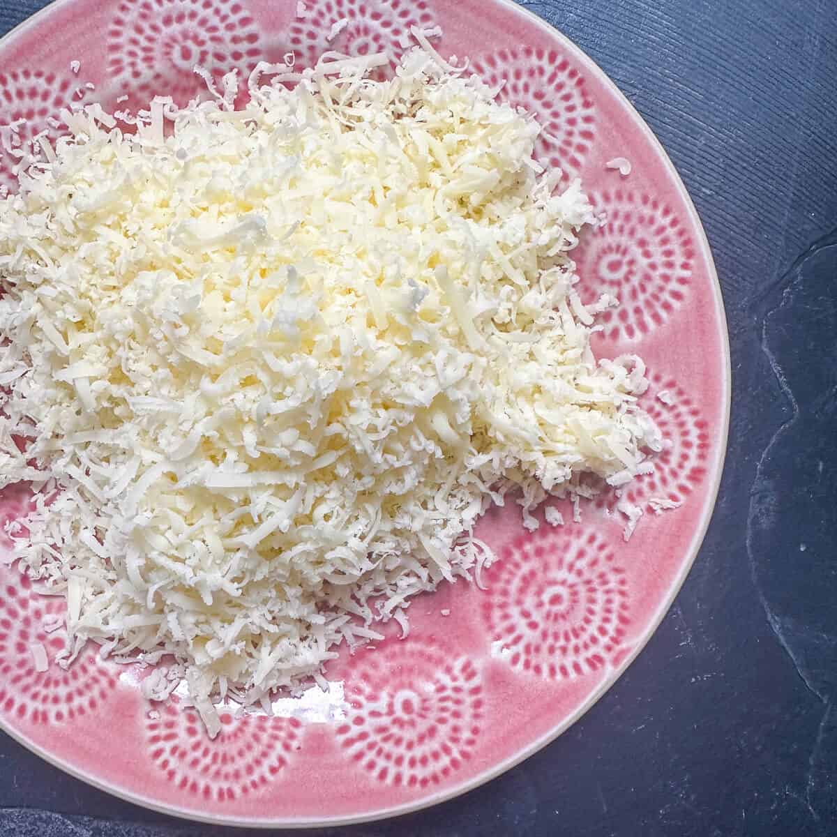 A mound of grated parmesan on a pink plate. 