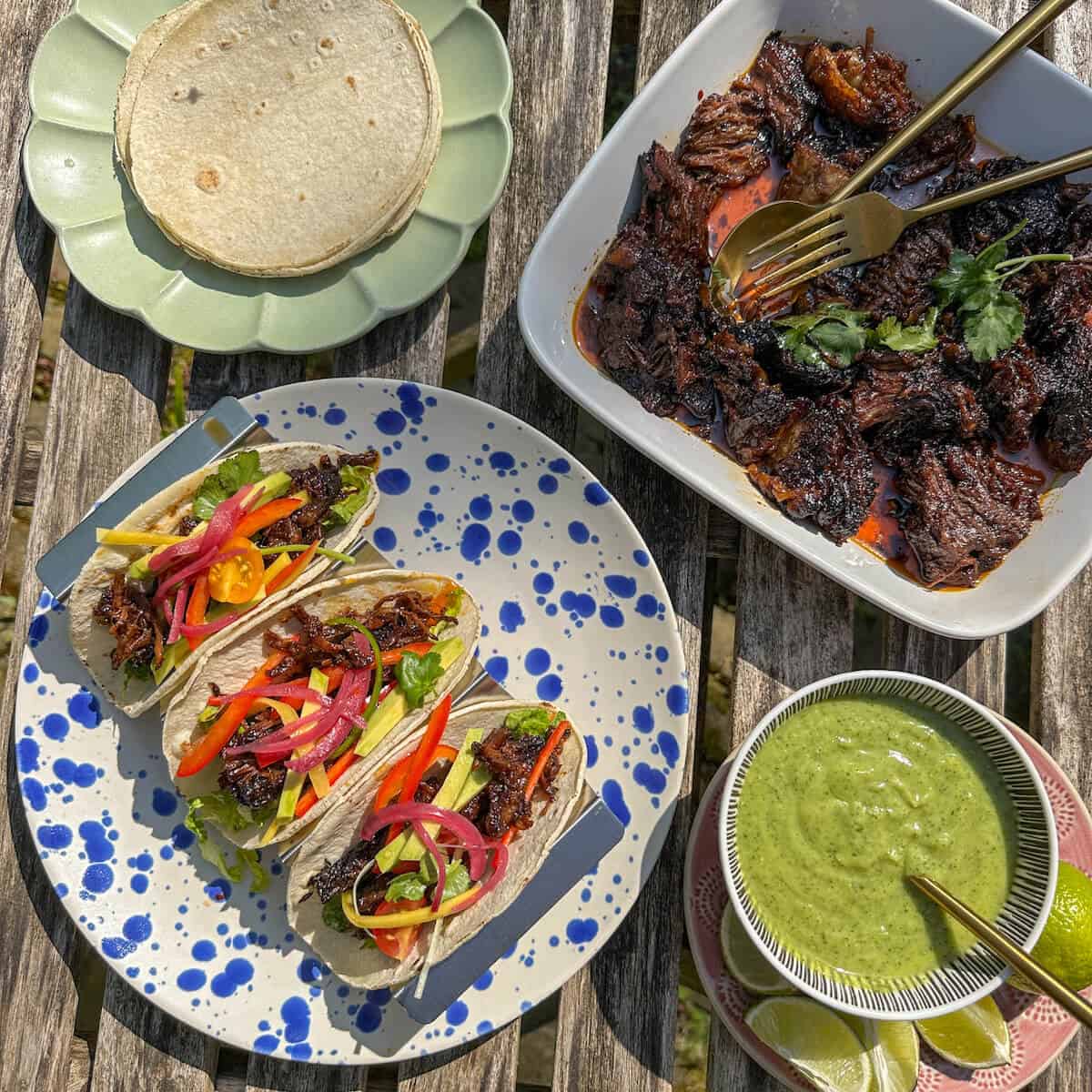 A table with tacos and a bowl of spicy lime avocado sauce. 