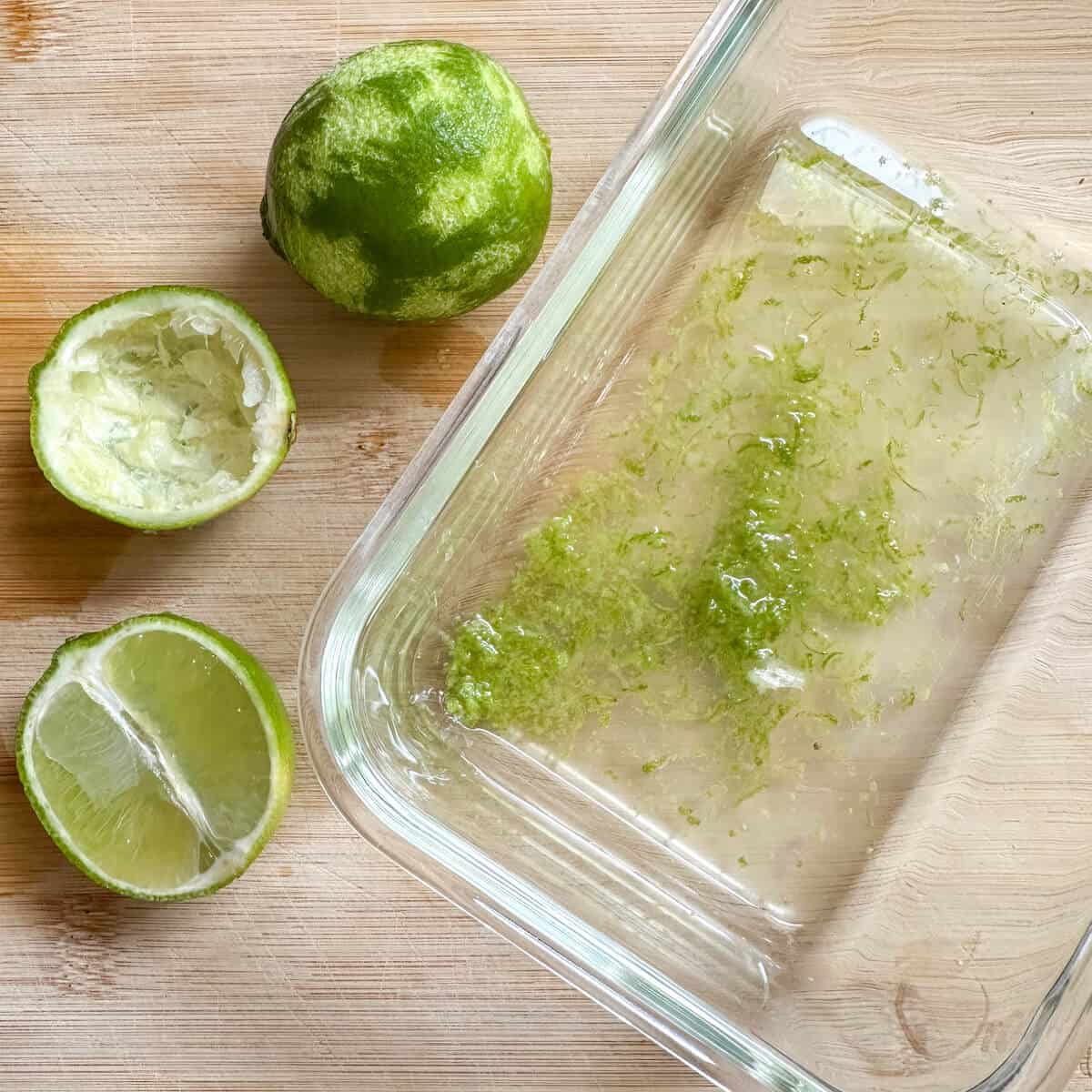 A glass bowl with lime juice and lime zest in, next to sliced limes. 