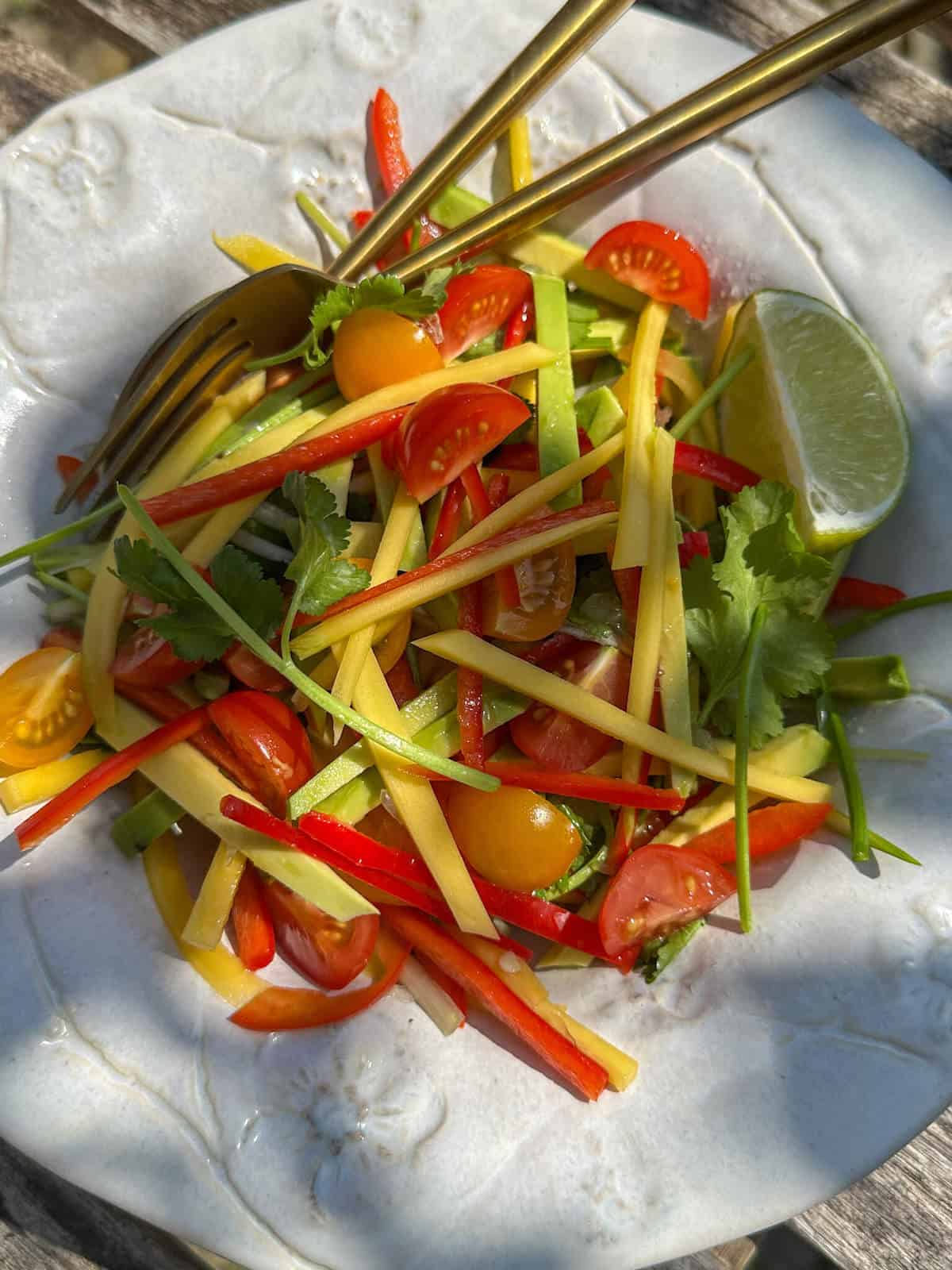 Spicy mango avocado salad in a bowl with serving utensils. 