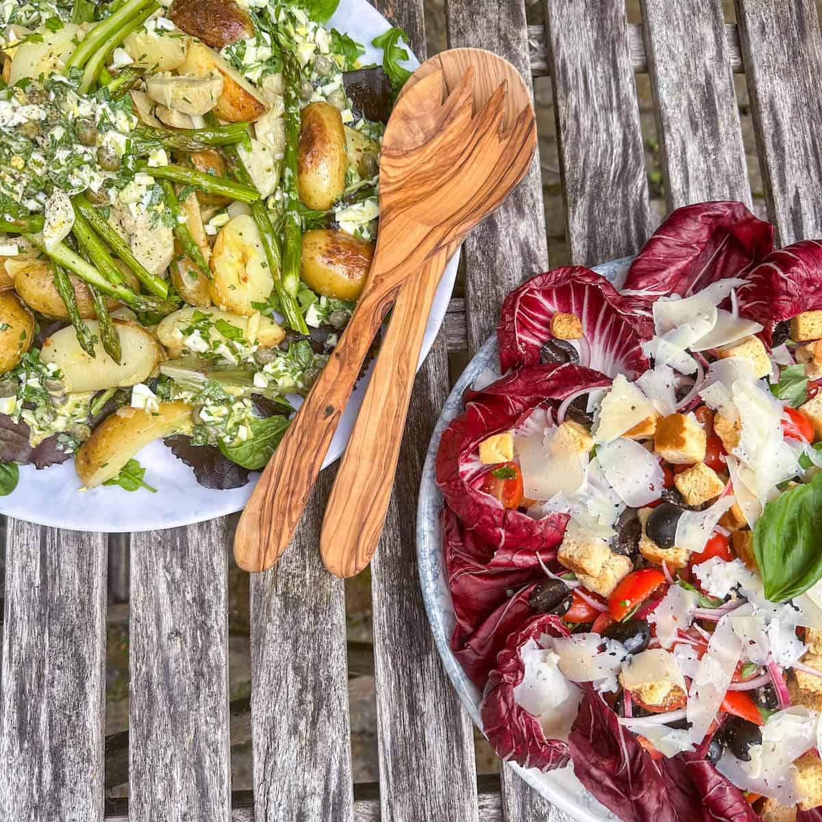 Artichoke, potato asparagus salad on a table next to another salad. 