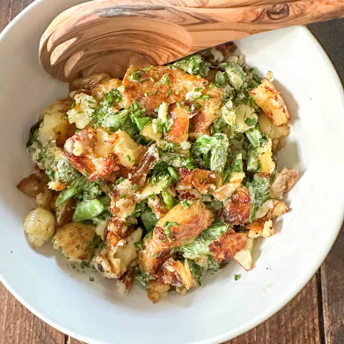 Crispy smashed potato salad in a bowl with serving utensils.