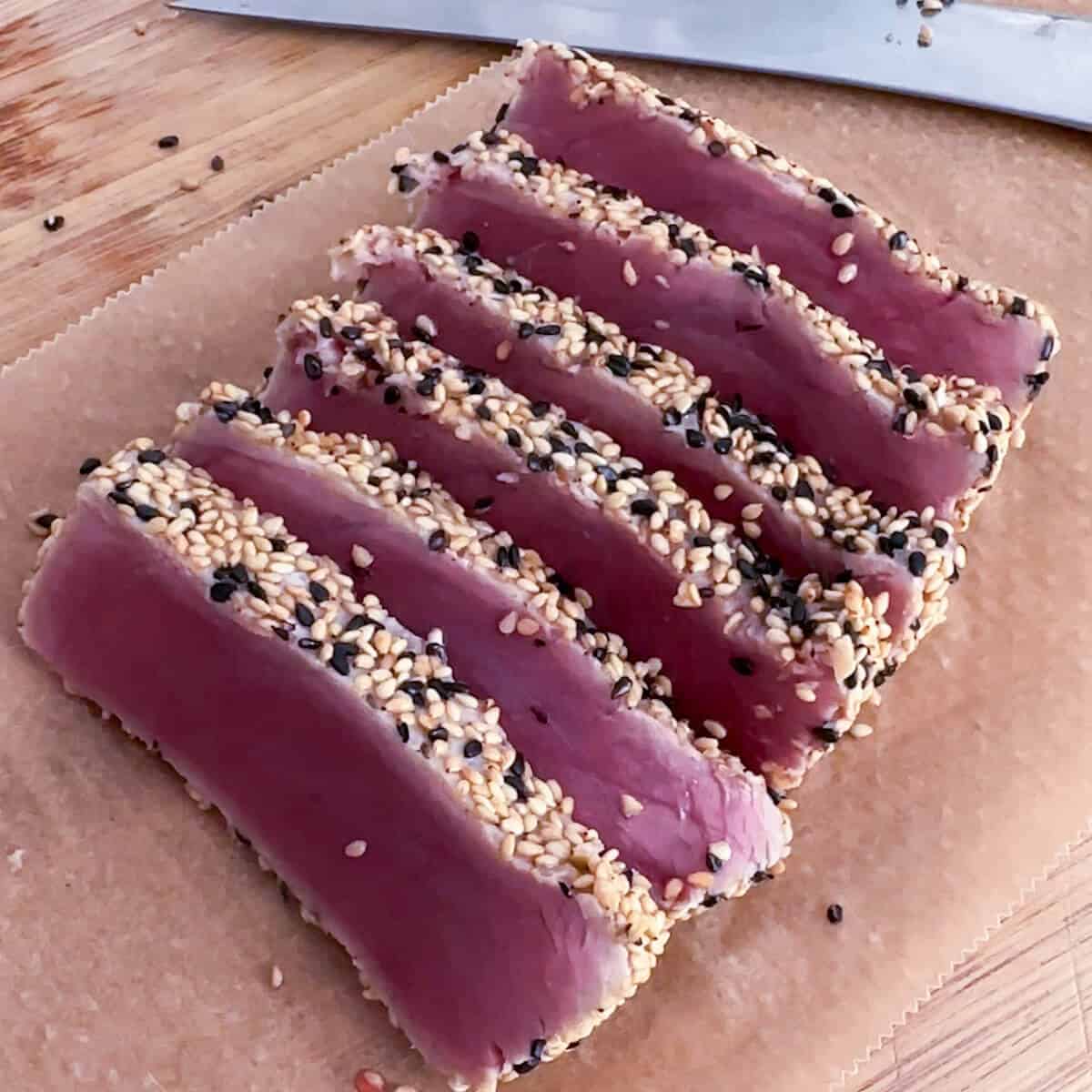 Sesame crusted tuna sliced into thin pieces on a chopping board. 