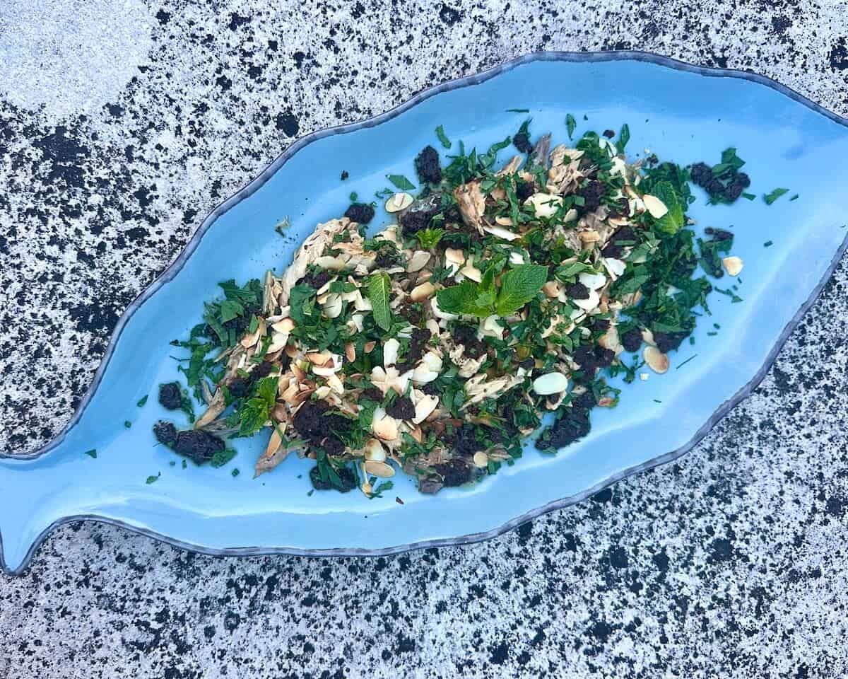 A platter of fire roasted tinned fish garnished with herbs, olives and almonds.