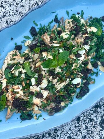 Fire roasted tinned fish on a platter with herbs, olives and almonds.