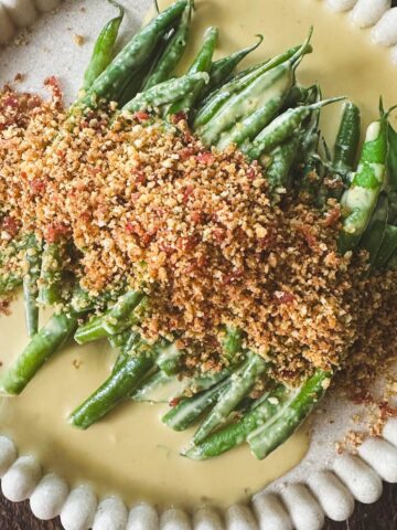 A plate of green beans covered in an anchovy cream sauce and a bacon panko breadcrumb topping.