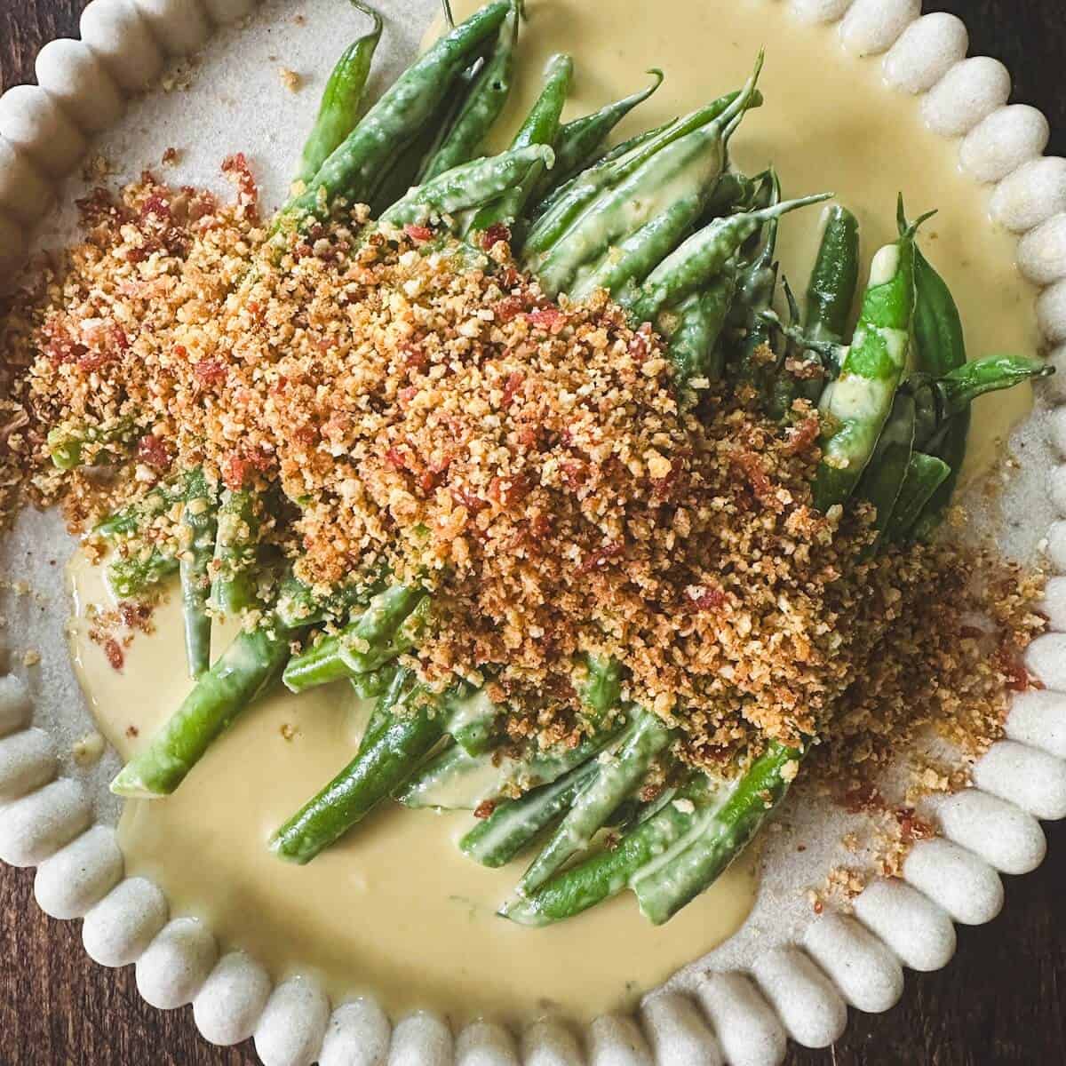 A plate of green beans covered in an anchovy cream sauce and a bacon panko breadcrumb topping.