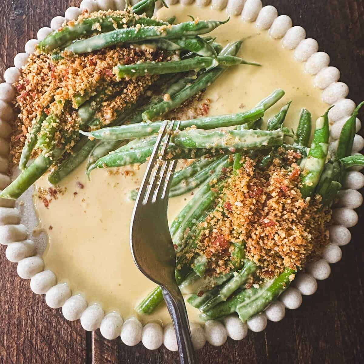 A fork holding green beans in anchovy cream sauce.