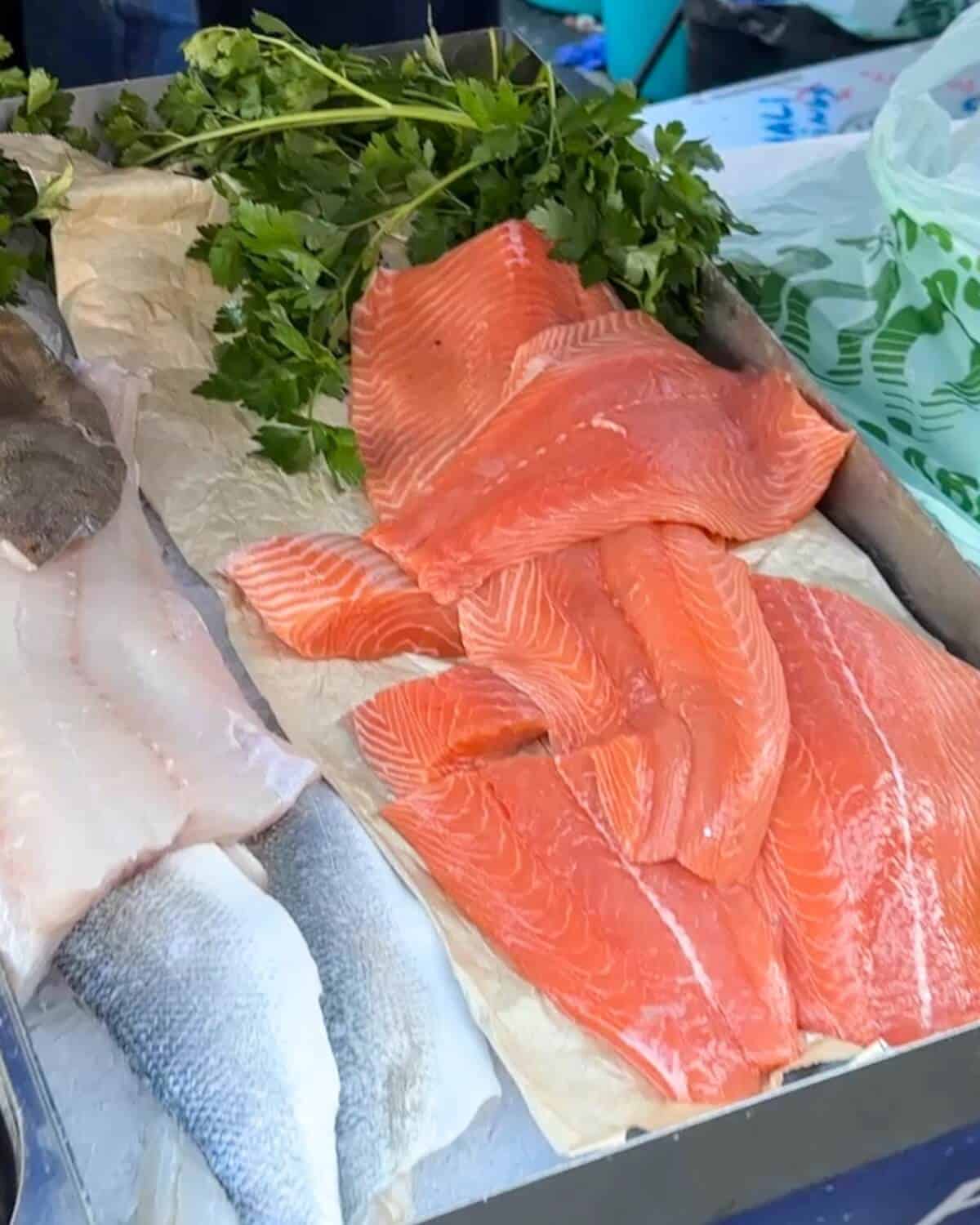 A fish stall at a market showing
whole sides of salmon for sale.