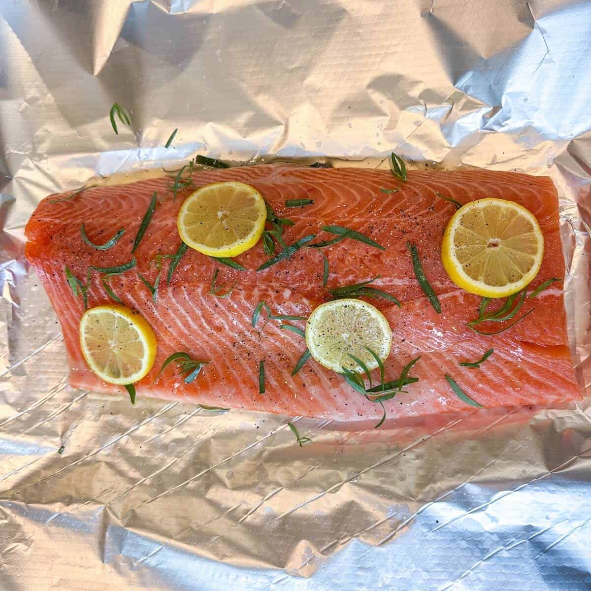 A side of salmon prepped for cooking with lemon and herbs.