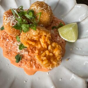 Gochujang arancini balls on top of a kimchi mayo sauce with wedge of lime and fresh herbs.