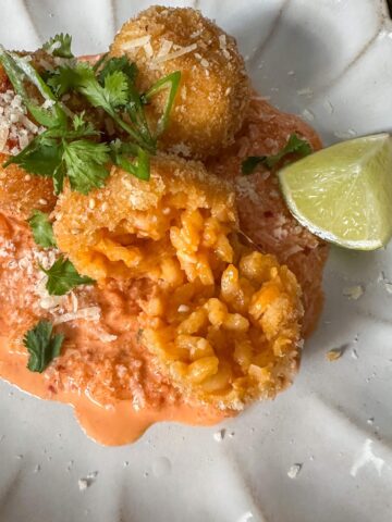 Gochujang arancini balls on top of a kimchi mayo sauce with wedge of lime and fresh herbs.