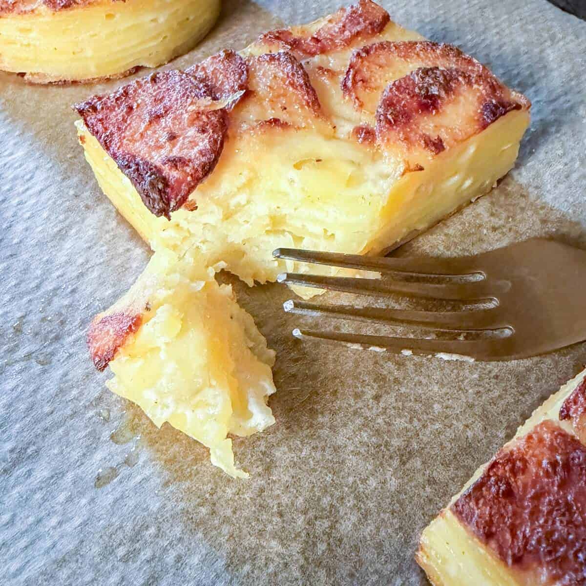 A slice of dauphinoise potatoes on a baking tray with a fork showing the layers.