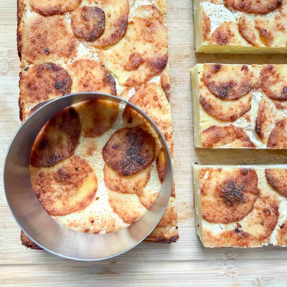 A block of baked potato dauphinoise being cut into shapes.