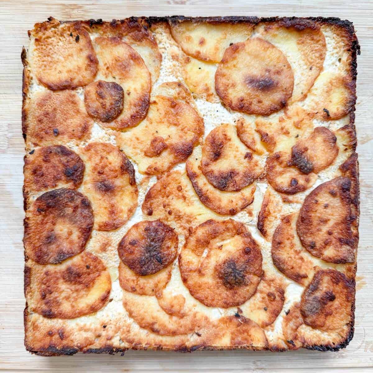 A cooked block of dauphinoise potatoes on a chopping board.