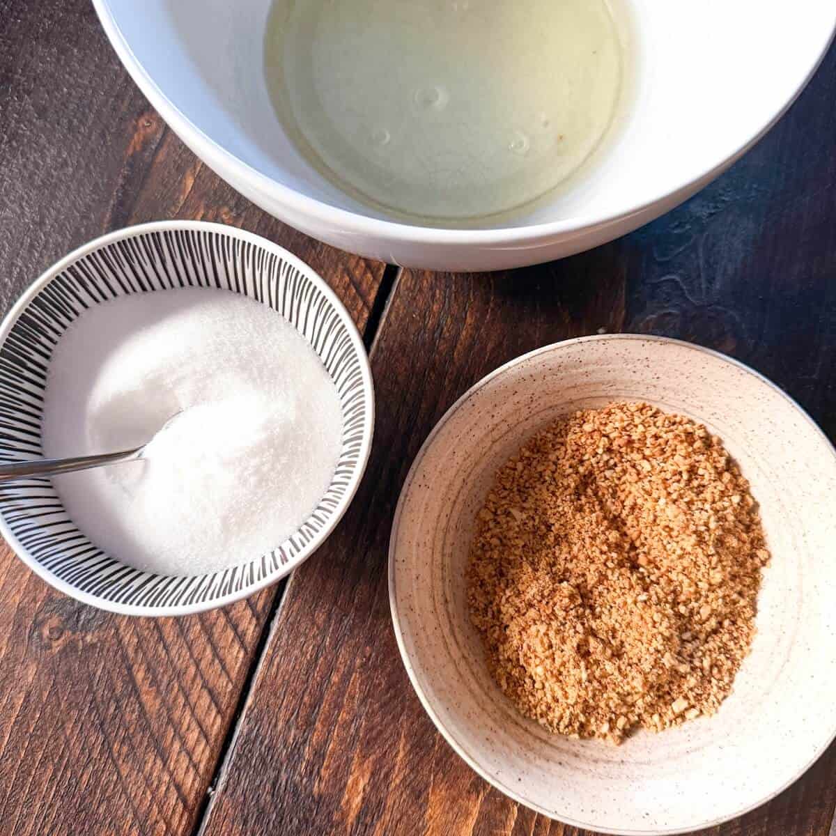 Ingredients for hazelnut meringue in bowls on a table. Ground toasted hazelnuts, granulated sugar, and egg whites.