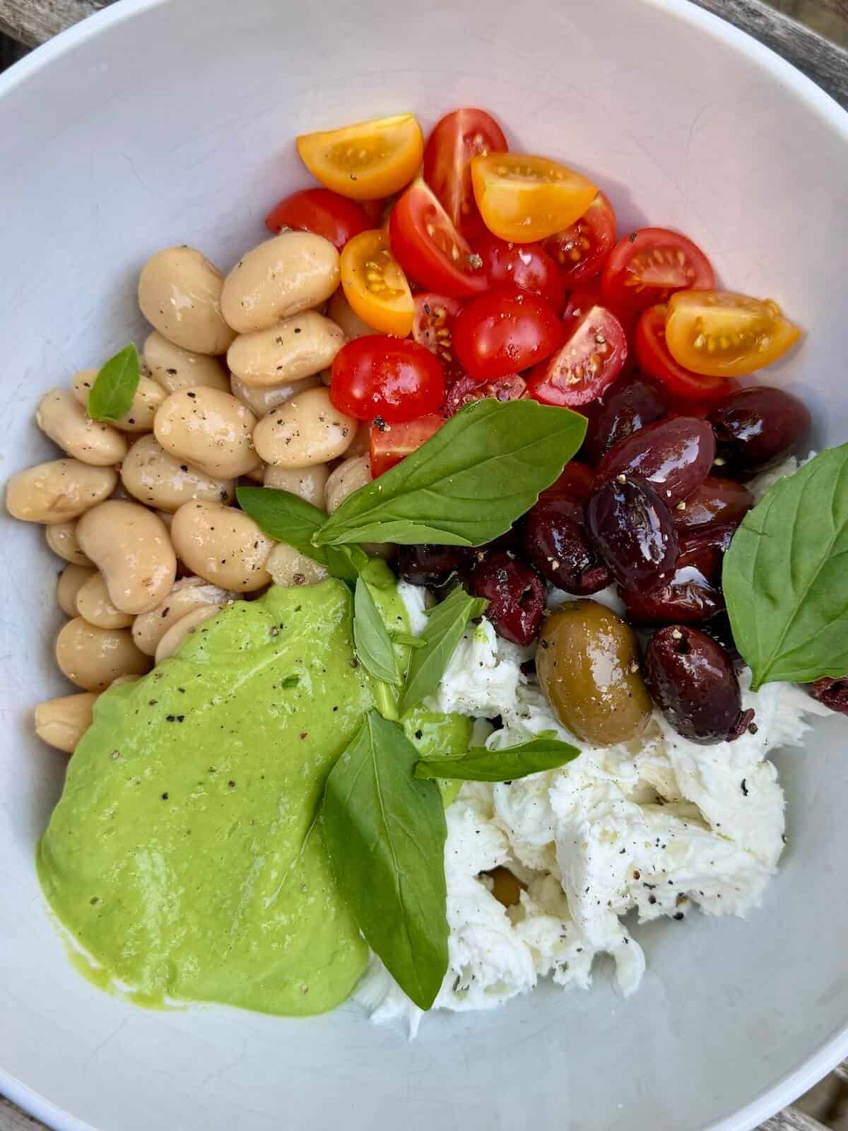 A salad bowl with the components of a caprese butterbean salad, ready to toss.