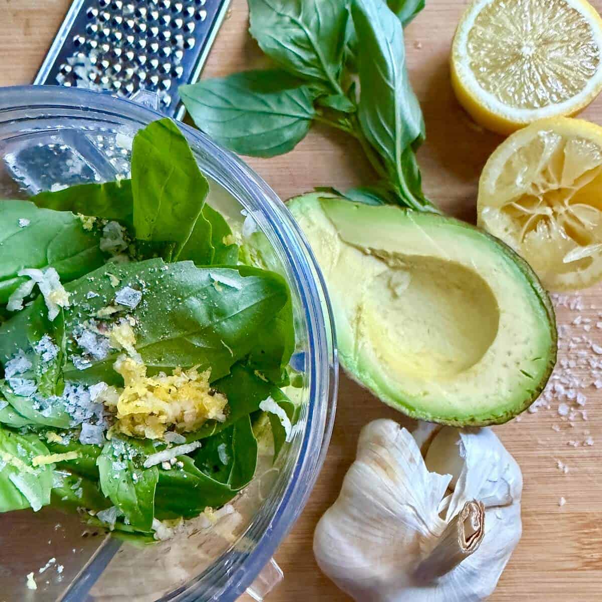 Ingredients for basil avocado dressing laid out on a wooden chopping board.