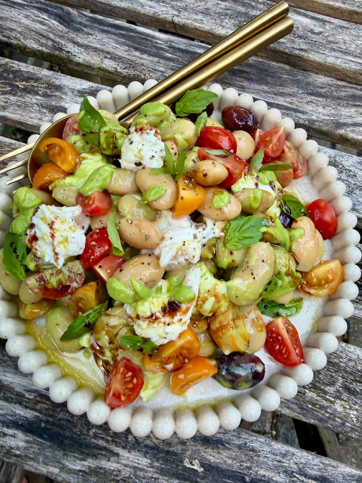 A plate of butterbean caprese salad with cherry tomatoes, olives, mozarella and a vibrant green basil vinaigrette.