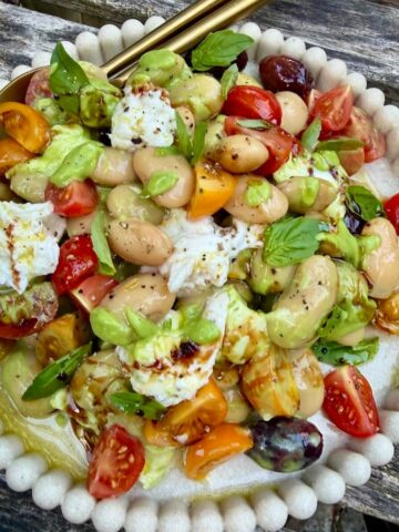 A plate of butterbean caprese salad with olives, tomato and mozzarella.